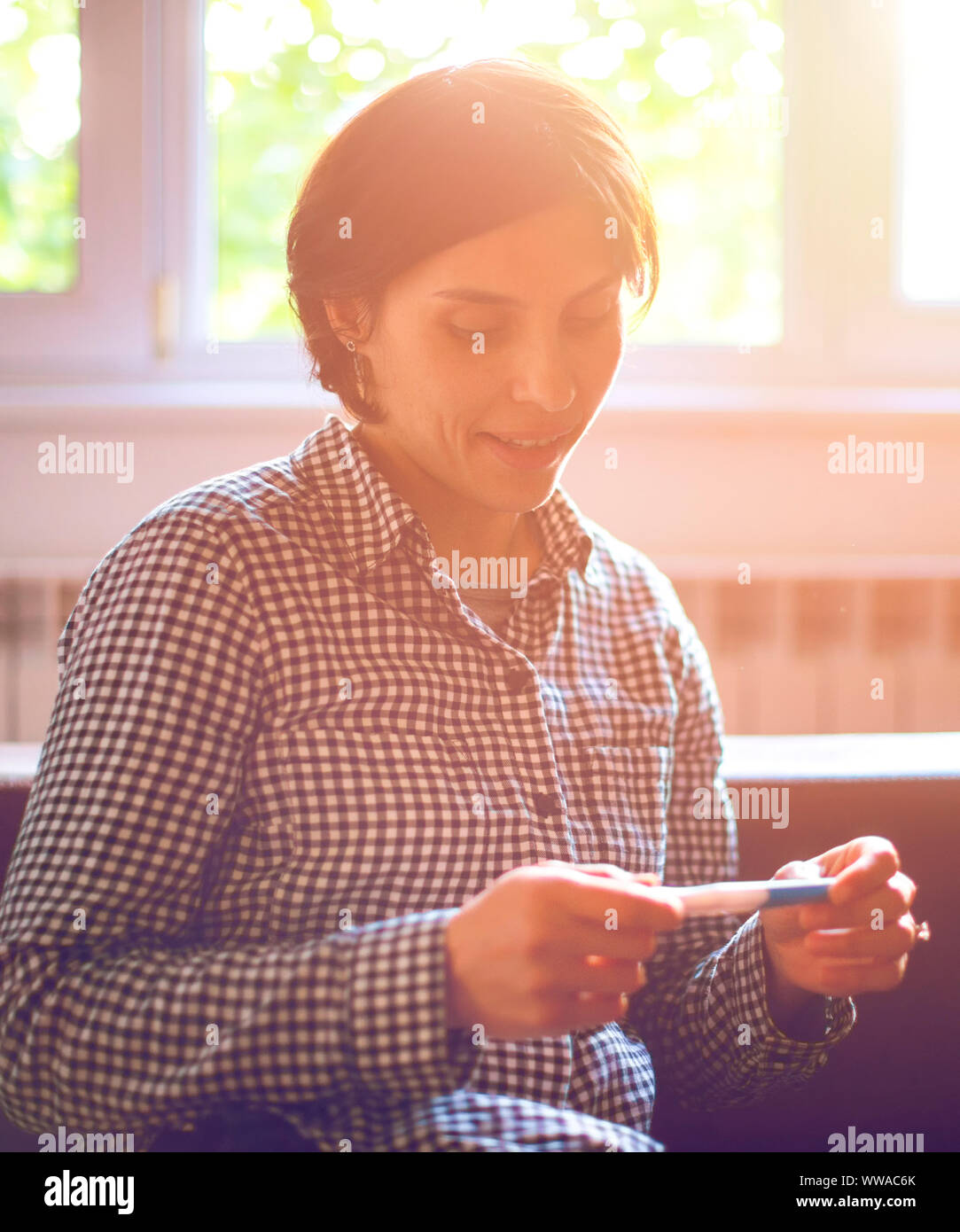 Infine incinta. Attraente di giovani donne guardando al test di gravidanza e sorridente comodamente seduti sul divano di casa Foto Stock