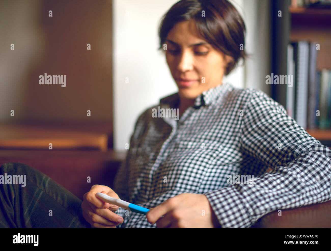 Infine incinta. Attraente di giovani donne guardando al test di gravidanza e sorridente comodamente seduti sul divano di casa Foto Stock