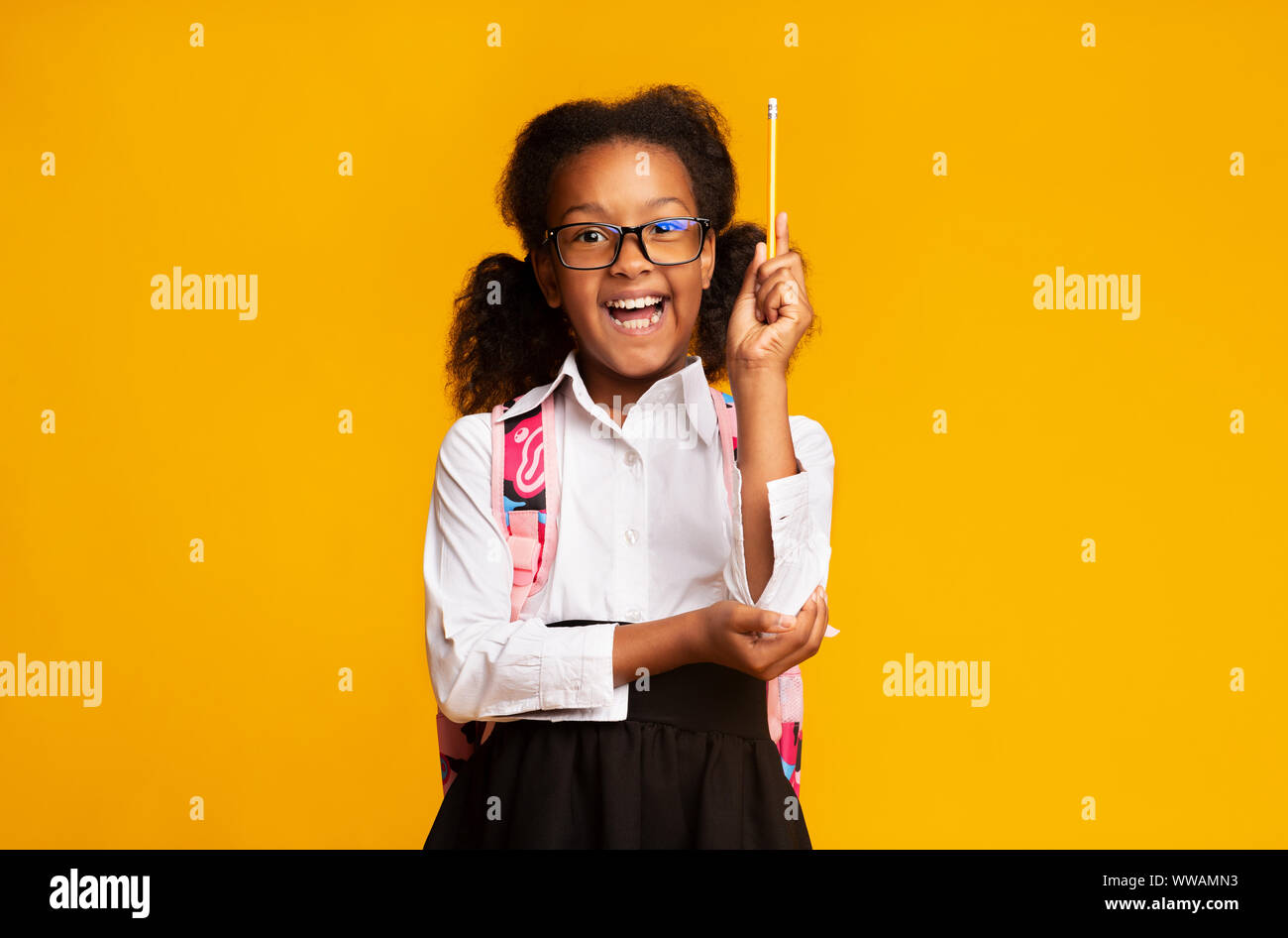 Felice Afro School girl alzando la mano tenendo premuto matita, sfondo giallo Foto Stock