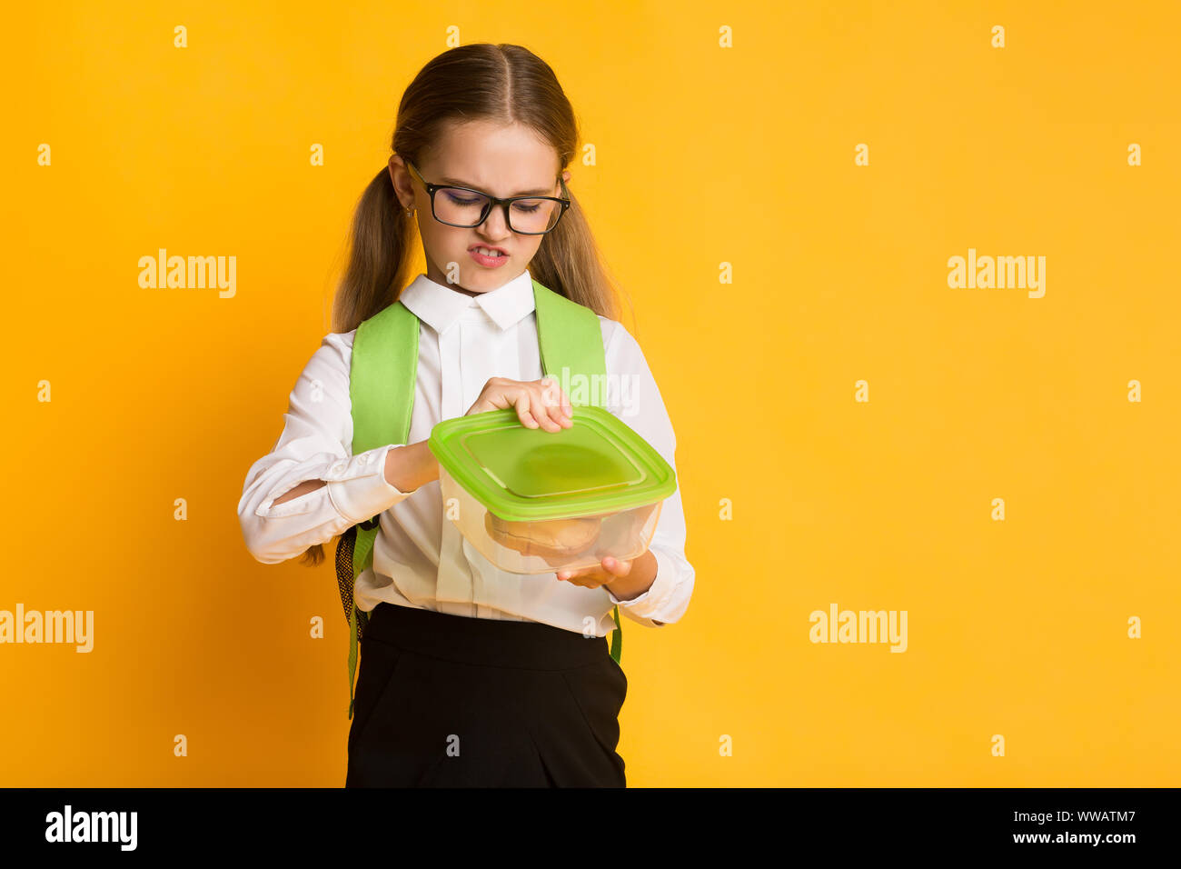 Disgustato Schoolgirl guardando a Sandwich In Lunchbox, sfondo giallo Foto Stock
