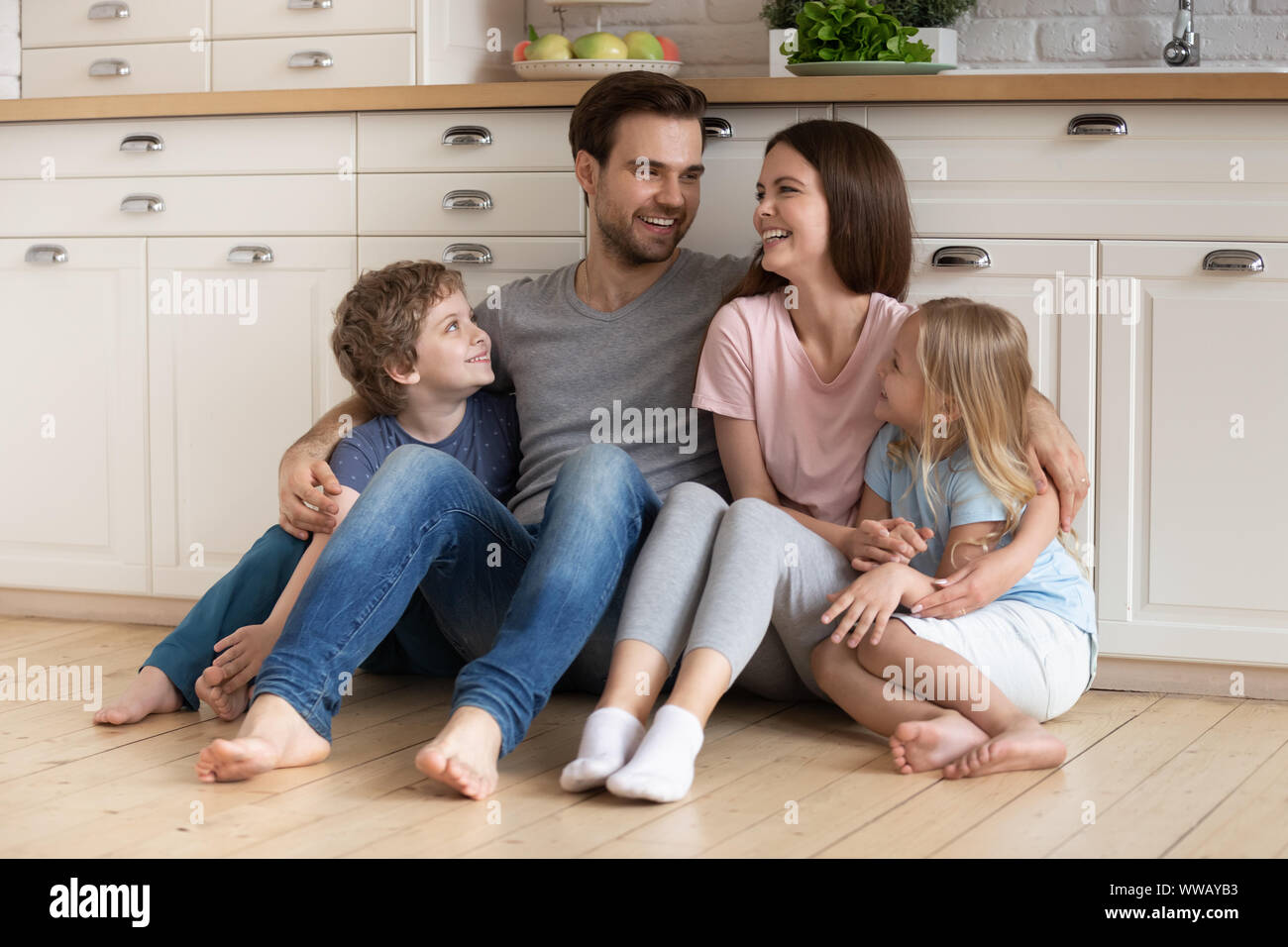 La famiglia felice di quattro seduti sul pavimento in legno in cucina. Foto Stock