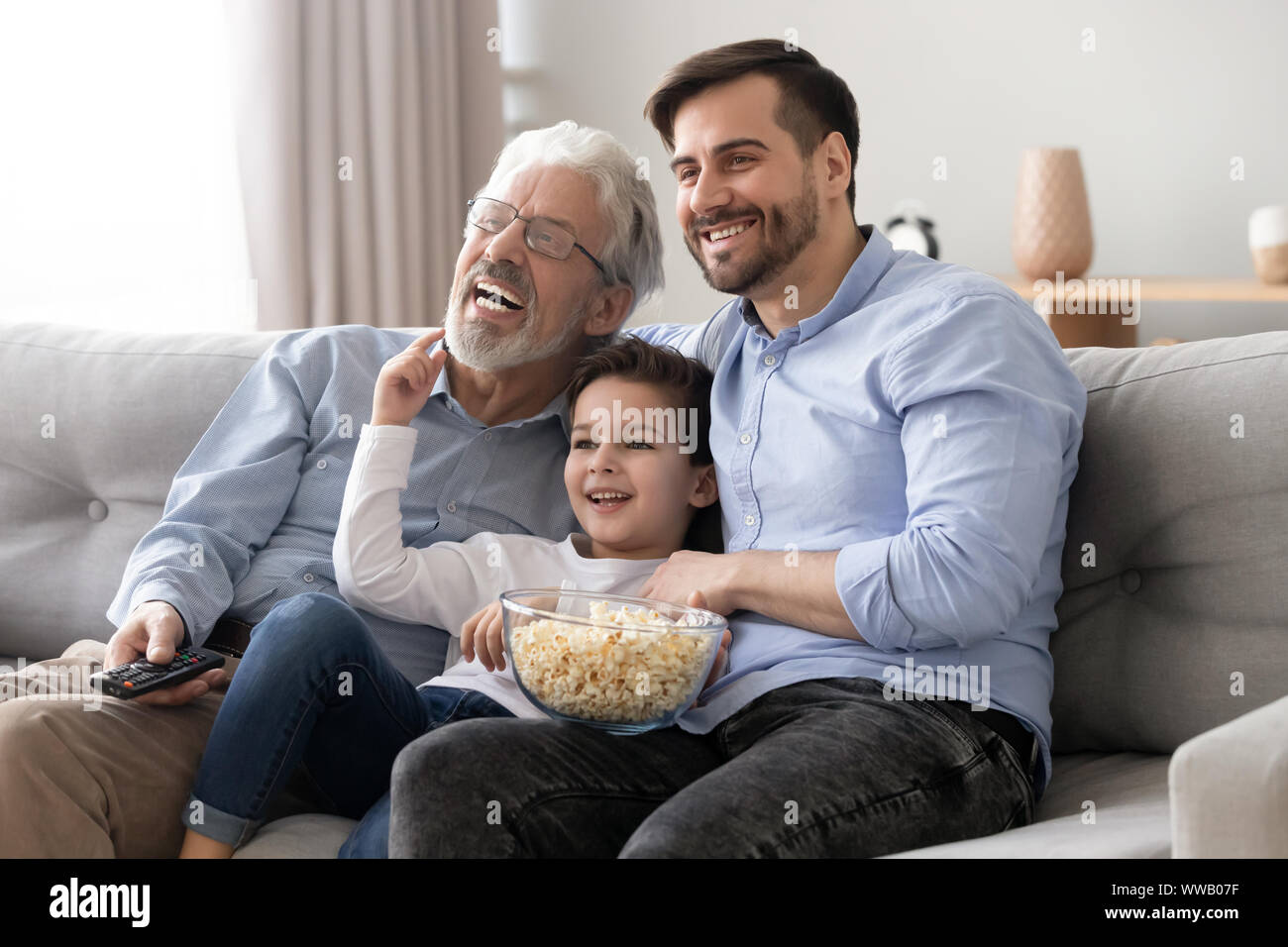 Felice tre generazioni di uomini famiglia tenere premuto il telecomando per guardare la tv Foto Stock