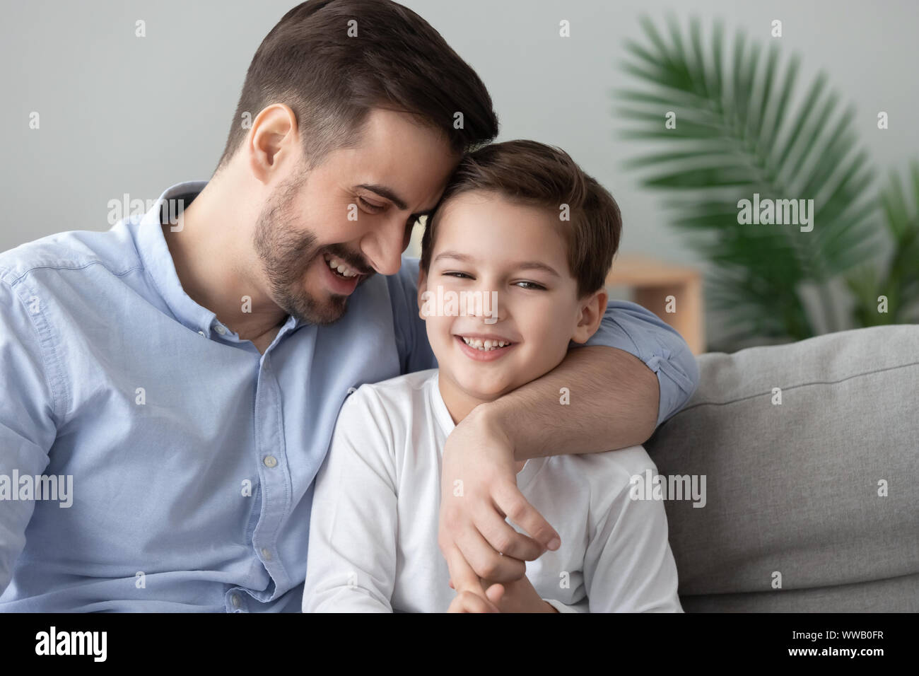 Affettuoso papà e figlio bambino incollaggio abbracciando sedere sul divano Foto Stock