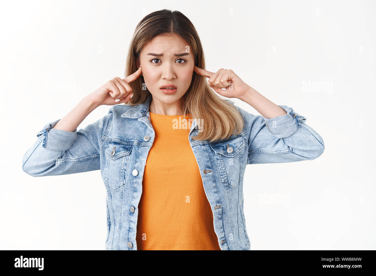 Timida Innocenzo sconvolto asian ragazza bionda non può stare a persone che lottano gridando accigliata nervosamente guardare fotocamera orecchie chiuse riluttante udire forti party rumoroso Foto Stock