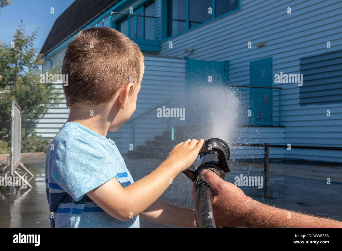 Un piccolo ragazzo la spruzzatura di acqua da una manichetta antincendio Foto Stock
