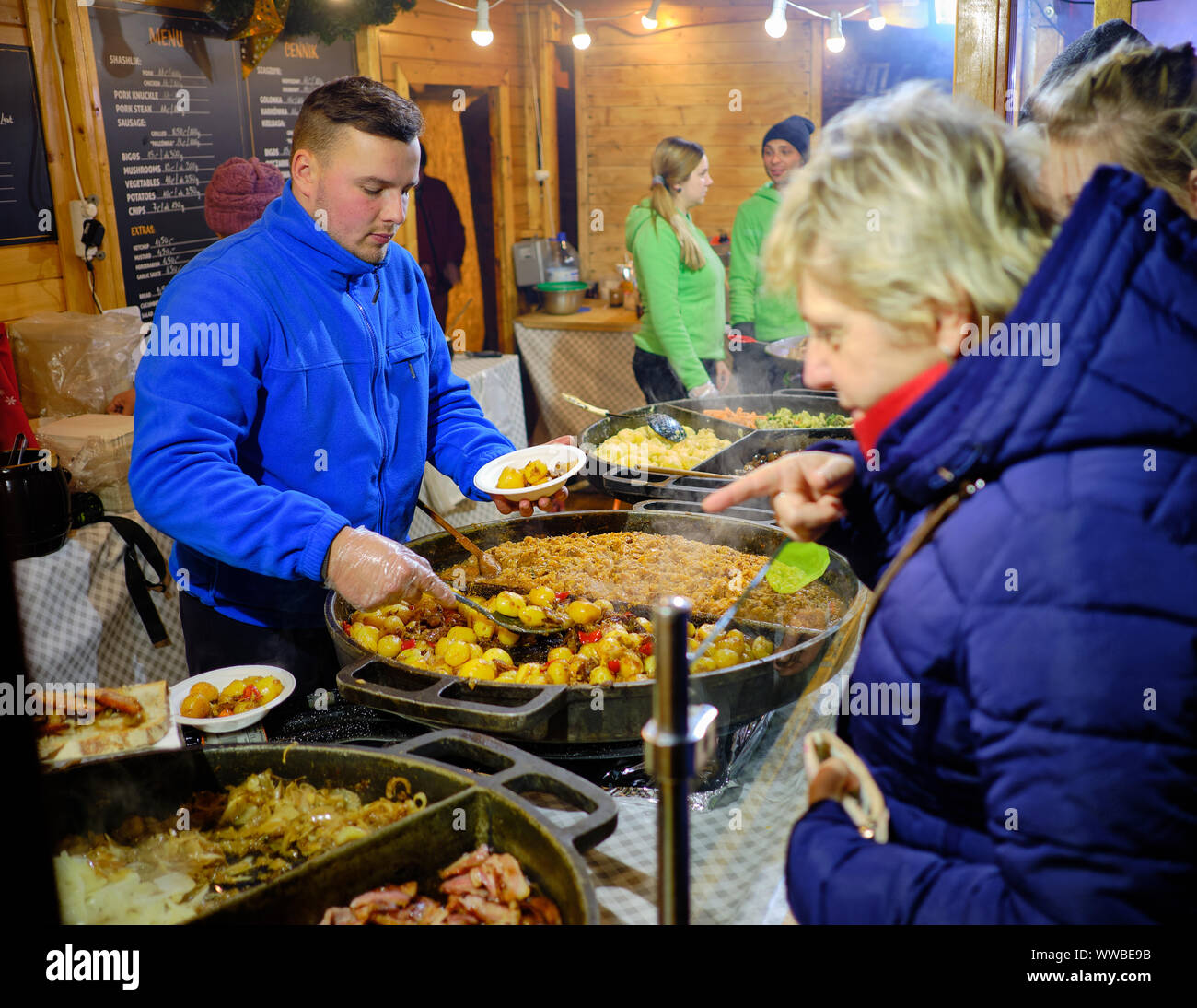 Wroclaw, Polonia Novembre 17, 2017. Maschio server alimentare incavature fuori piatti tradizionali polacchi in stallo alimentare durante il Mercatino di Natale di notte Foto Stock