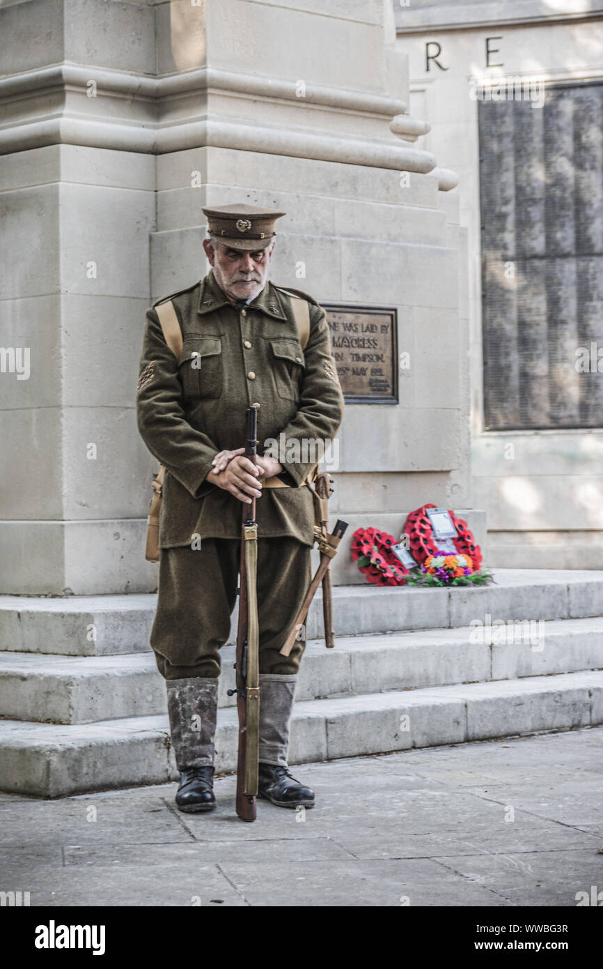 Un uomo in guerra mondiale una uniforme di soldati in piedi accanto a un British war memorial con papavero rosso ghirlande prevista su di esso Foto Stock