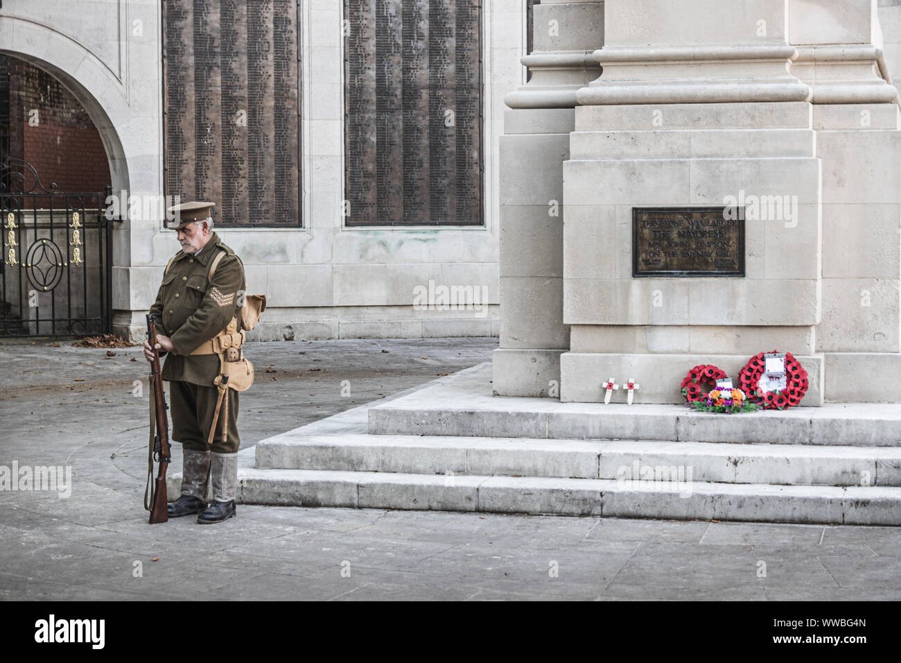 Un uomo in guerra mondiale una uniforme di soldati in piedi accanto a un British war memorial con papavero rosso ghirlande prevista su di esso Foto Stock