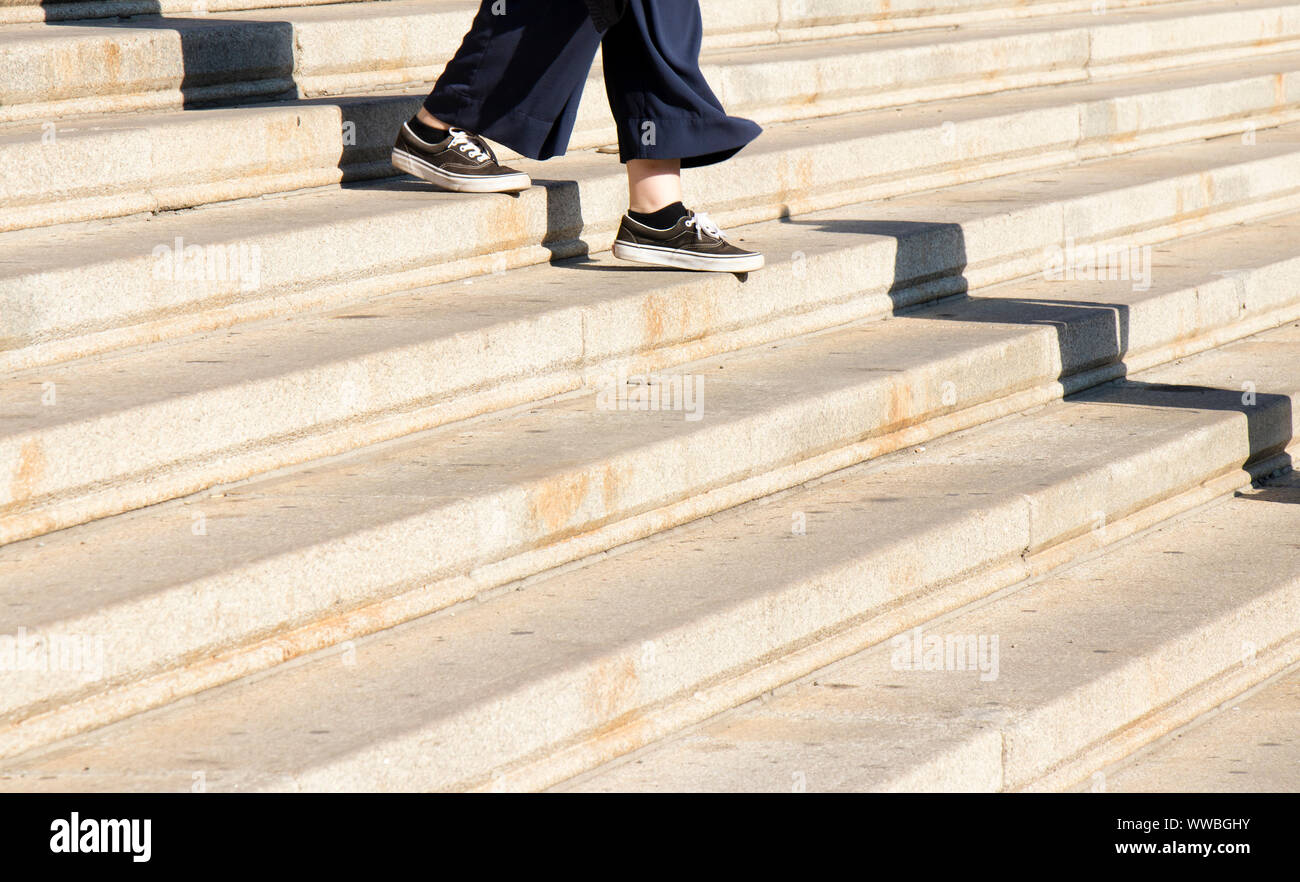Le gambe della giovane donna in sneaker scarpe camminando giù le scale della città in una giornata di sole Foto Stock