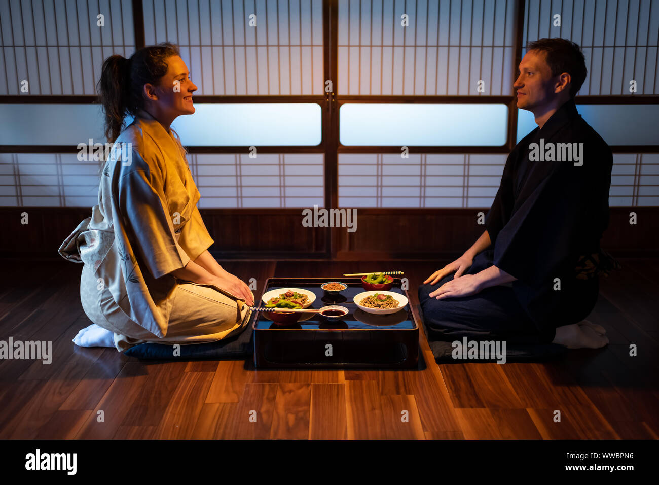 Giovani sorridenti giovane seiza seduti su cuscini a terra con tradizionale giapponese ryokan piatti kaiseki di Soba Noodles, natto, edamame e soia sauc Foto Stock