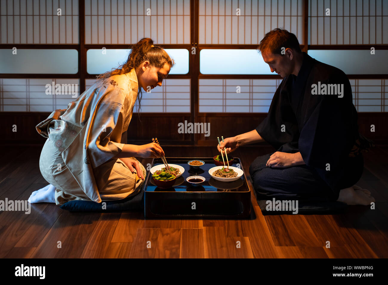 Coppia giovane seiza seduti su cuscini a terra con il Giapponese ryokan piatti kaiseki, Mangiare Soba Noodles, natto, edamame e salsa di soia sul tavolo da shoji s Foto Stock