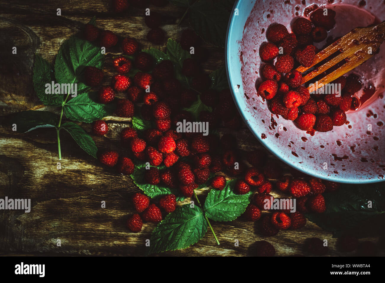 Rosso dei lamponi freschi su marrone legno rustico sfondo. Ciotola con maturazione naturale di bacche organiche con peduncoli, foglie verdi e legno forcella, vista dall'alto, Foto Stock