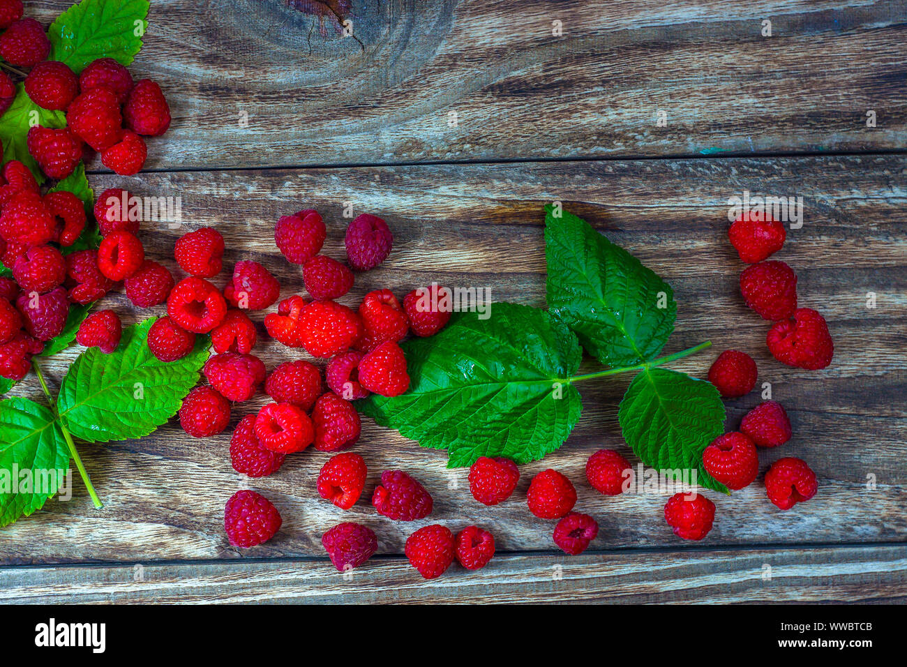 Rosso dei lamponi freschi su un legno rustico sfondo. Maturazione naturale di bacche organiche con peduncoli foglie verdi, vista dall'alto, laici piatta con copia spazio. Foto Stock