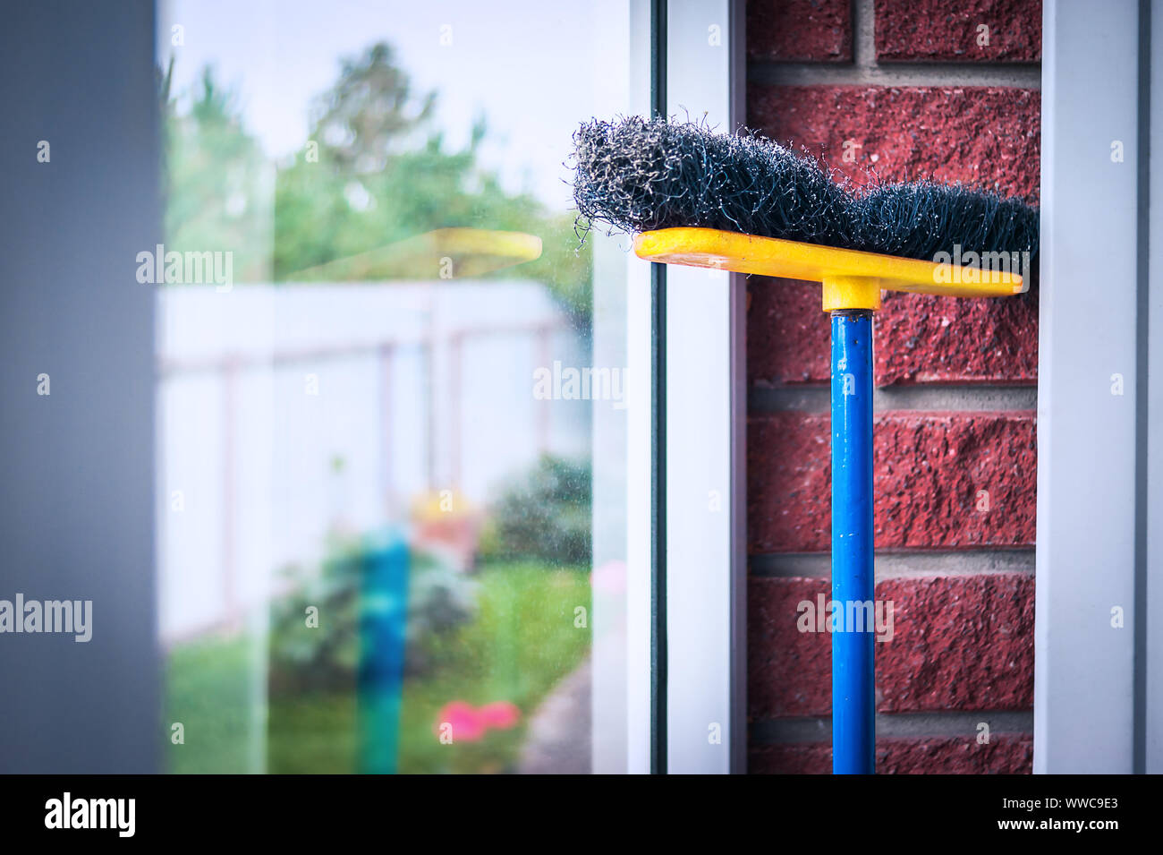 Giallo, Blu e nero poli spingere la scopa appoggiata contro il vetro e mattoni rossi nel muro della stanza di fango. Mantenere l'ambiente pulito e ordinato concetto. Foto Stock