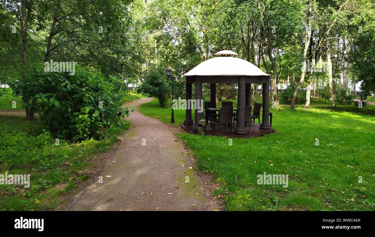 Sentiero in ghiaia nella verde foresta estiva che conduce ad un gazebo in legno per la preparazione della griglia Foto Stock