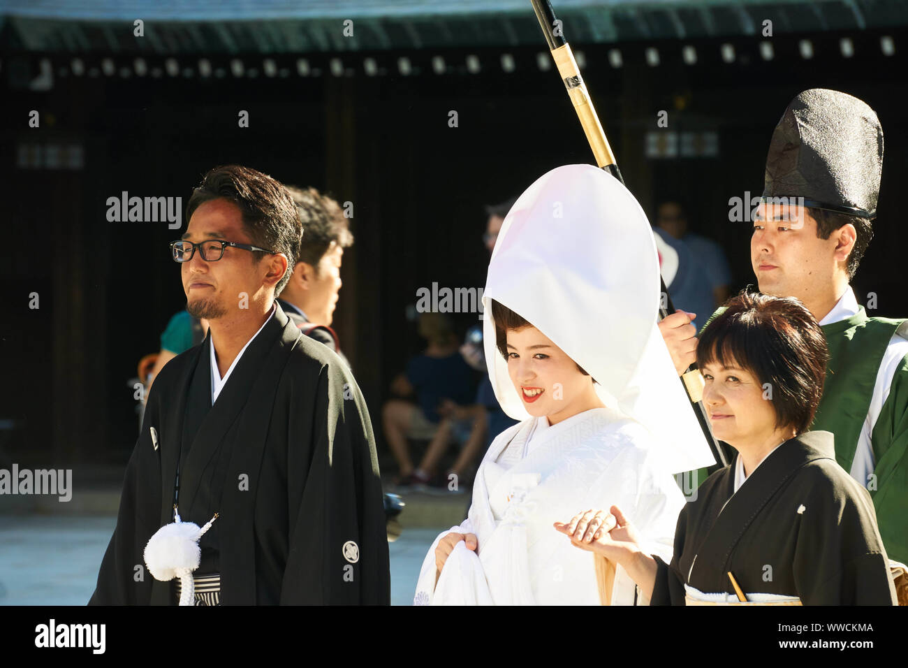 Una sposa in bianco e uno sposo in nero formale kimono camminare sotto un grande ombrello durante la tradizionale cerimonia di nozze Shinto al Santuario Meiji Jingu. Foto Stock
