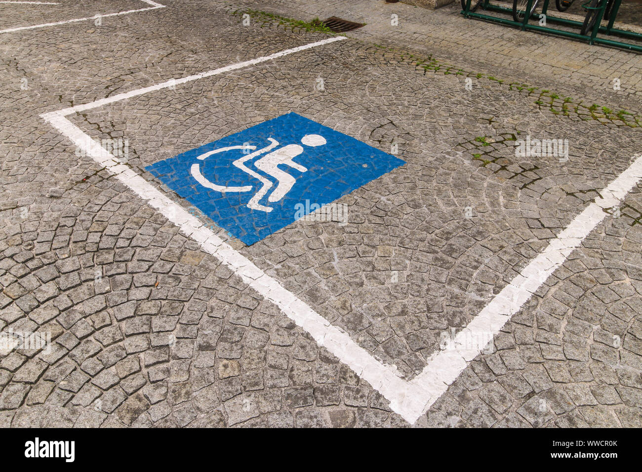 Accessibile spazio parcheggio riservato per le persone con disabilità. Quadrato blu con una persona in carrozzina dipinta su una pavimentazione di ciottoli Foto Stock