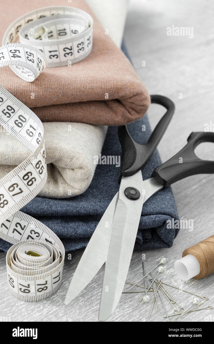Tessuti e articoli di cucitura: sartoria forbici, nastro di misurazione, lo stelo del thread, compresi i pin per cucire vestiti. su un tavolo. Foto Stock