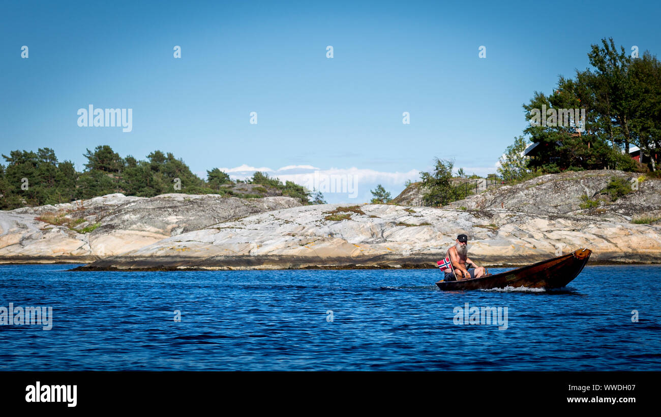 L'uomo la vela un dinghy in legno fuori Korset a Skatoy in Norvegia, dotato di un 5hp motore fuoribordo. Il design è tipica per il piccolo norvegese barche in legno. Foto Stock