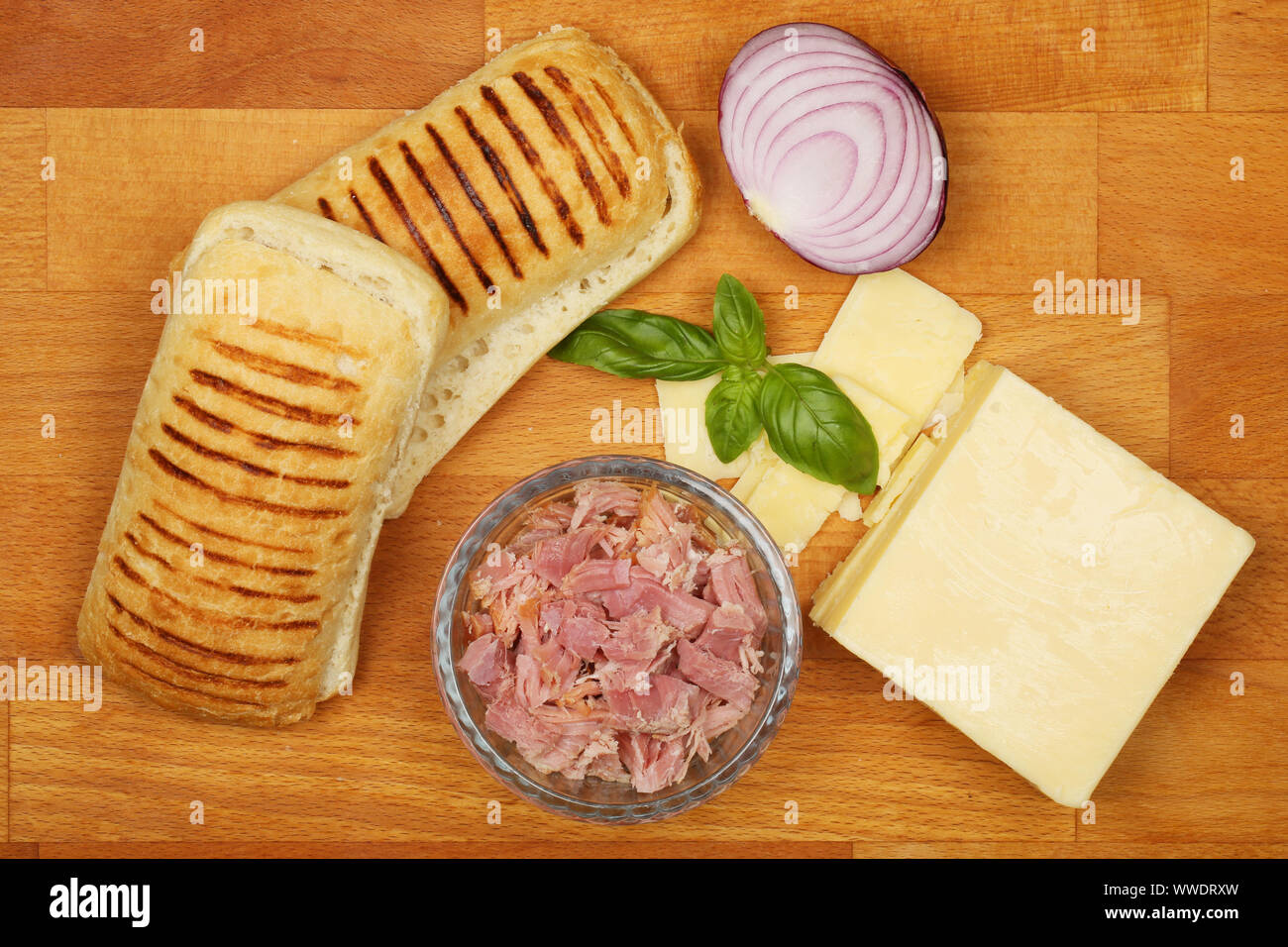 Panini e gli ingredienti, formaggio, prosciutto cotto, cipolla rossa e basilico su un tagliere di legno Foto Stock