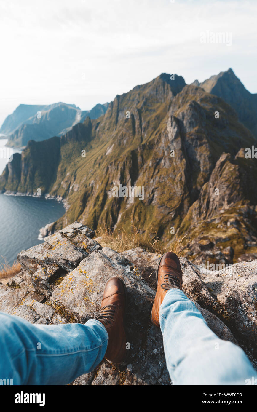 Viaggiatore Da Solo seduto sul bordo della montagna sopra il mare. POV vista sulle grandi montagne e scarponcini da trekking. Foto Stock