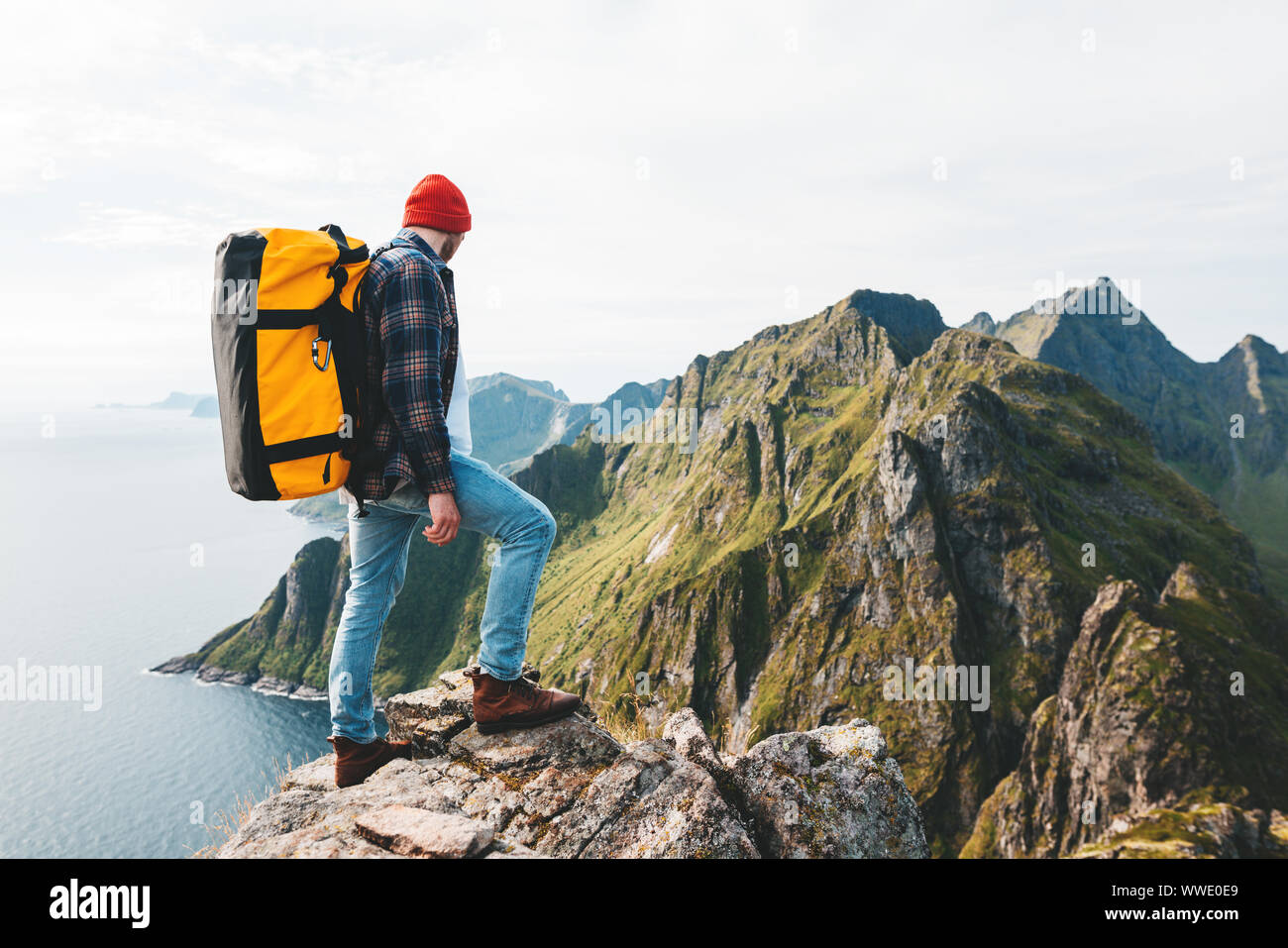 Traveler uomo che indossa uno zaino e Red Hat salire in alta montagna sopra il mare. Professional expeditor in piedi sul bordo della scogliera e rock cercando forwar Foto Stock