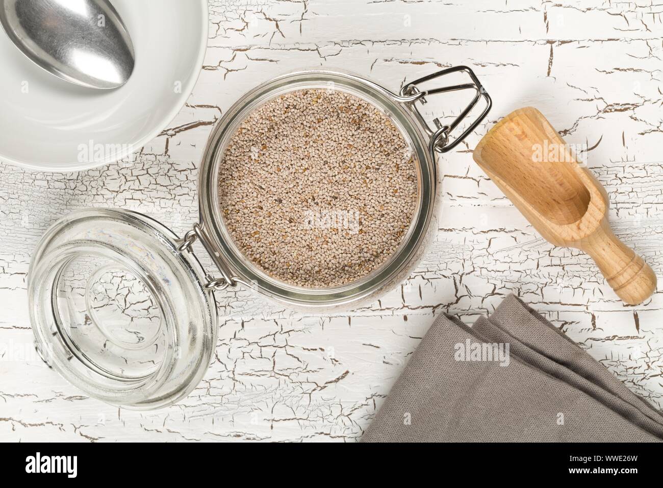 Tutto, organico bianco semi di chia mucchio nel vetro vaso di storage su bianco rustico sfondo tabella con paletta di legno e ciotola vista superiore piatta da laici al di sopra Foto Stock