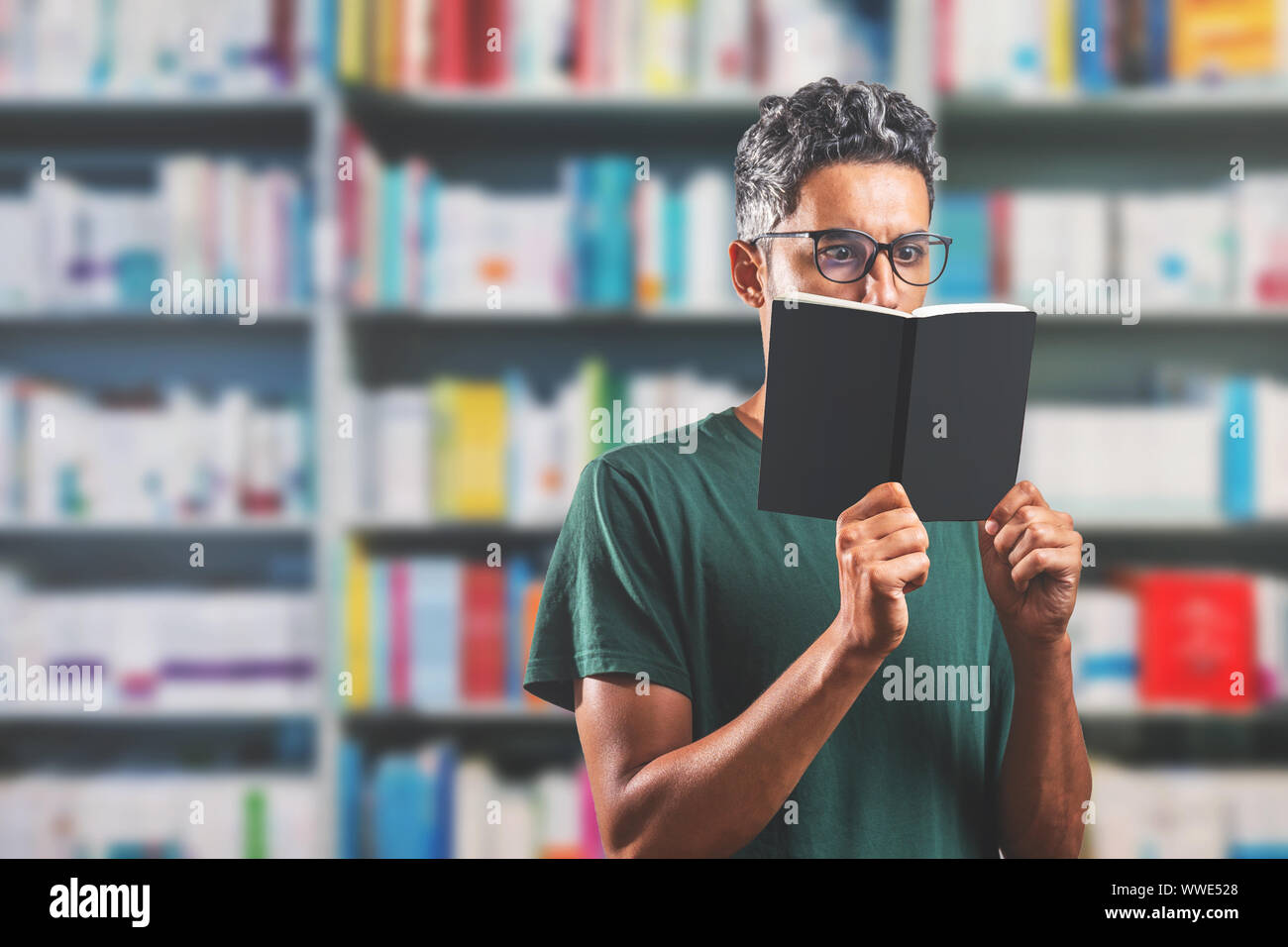 Uomo che indossa gli occhiali per leggere un libro nella biblioteca - profondità di campo - libro bianco - Spazio per il testo Foto Stock