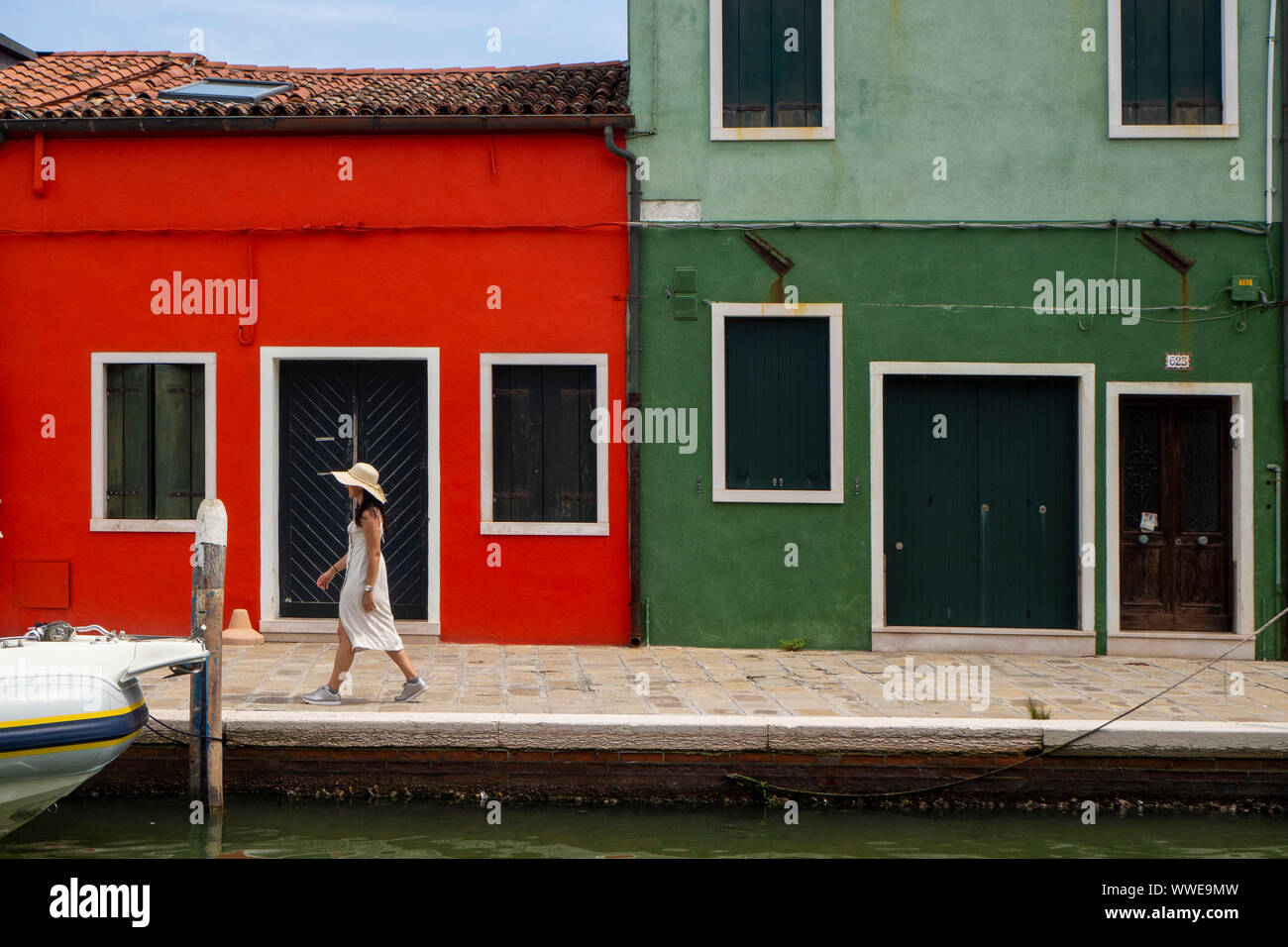 Turistico con cappello e abito da solo a piedi attraverso i canali di Burano e per le sue pittoresche case.. Venezia. Foto Stock