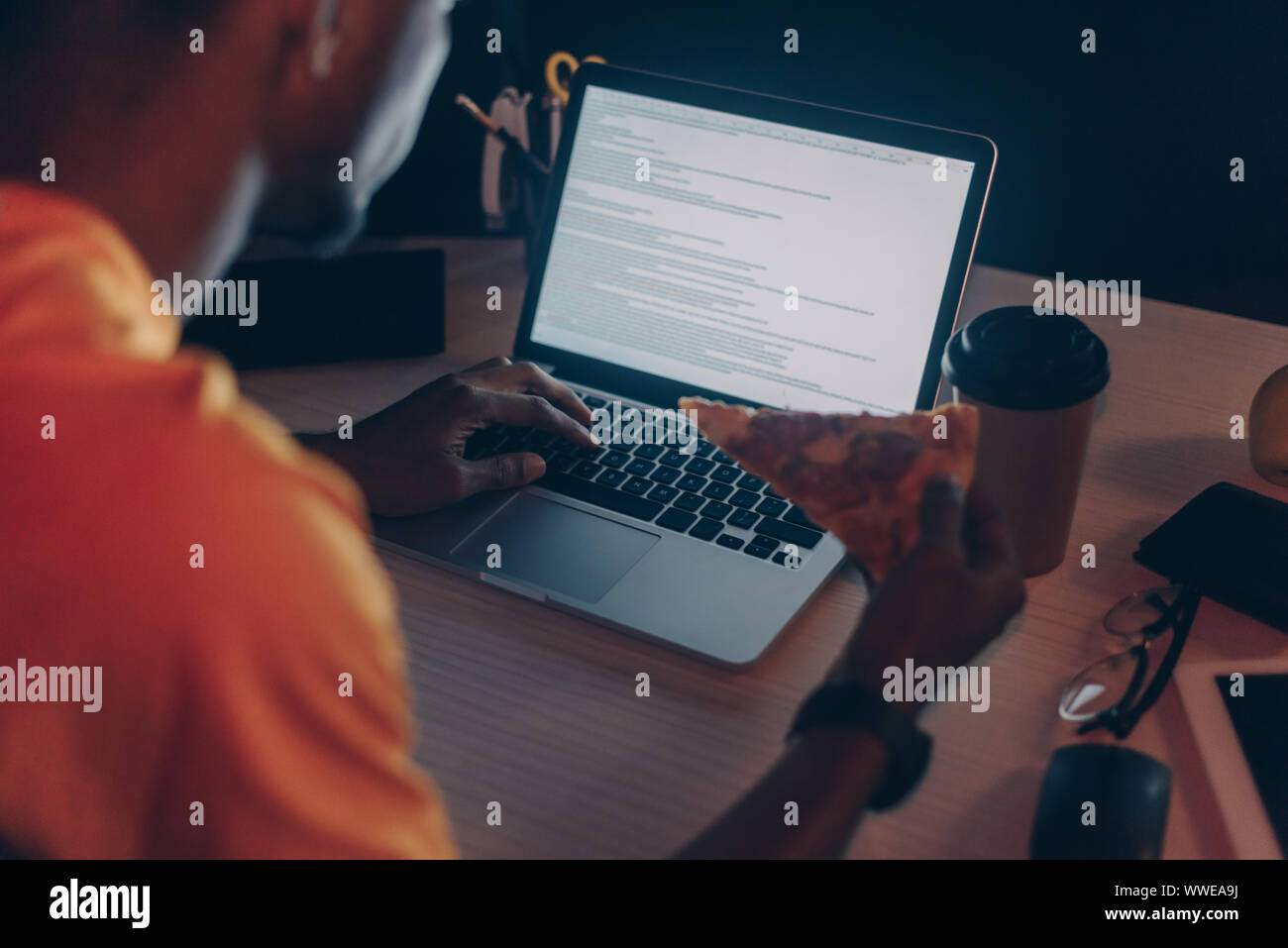 Vista ritagliata di giovani africani programmatore americano di mangiare la pizza durante il lavoro notturno in ufficio Foto Stock
