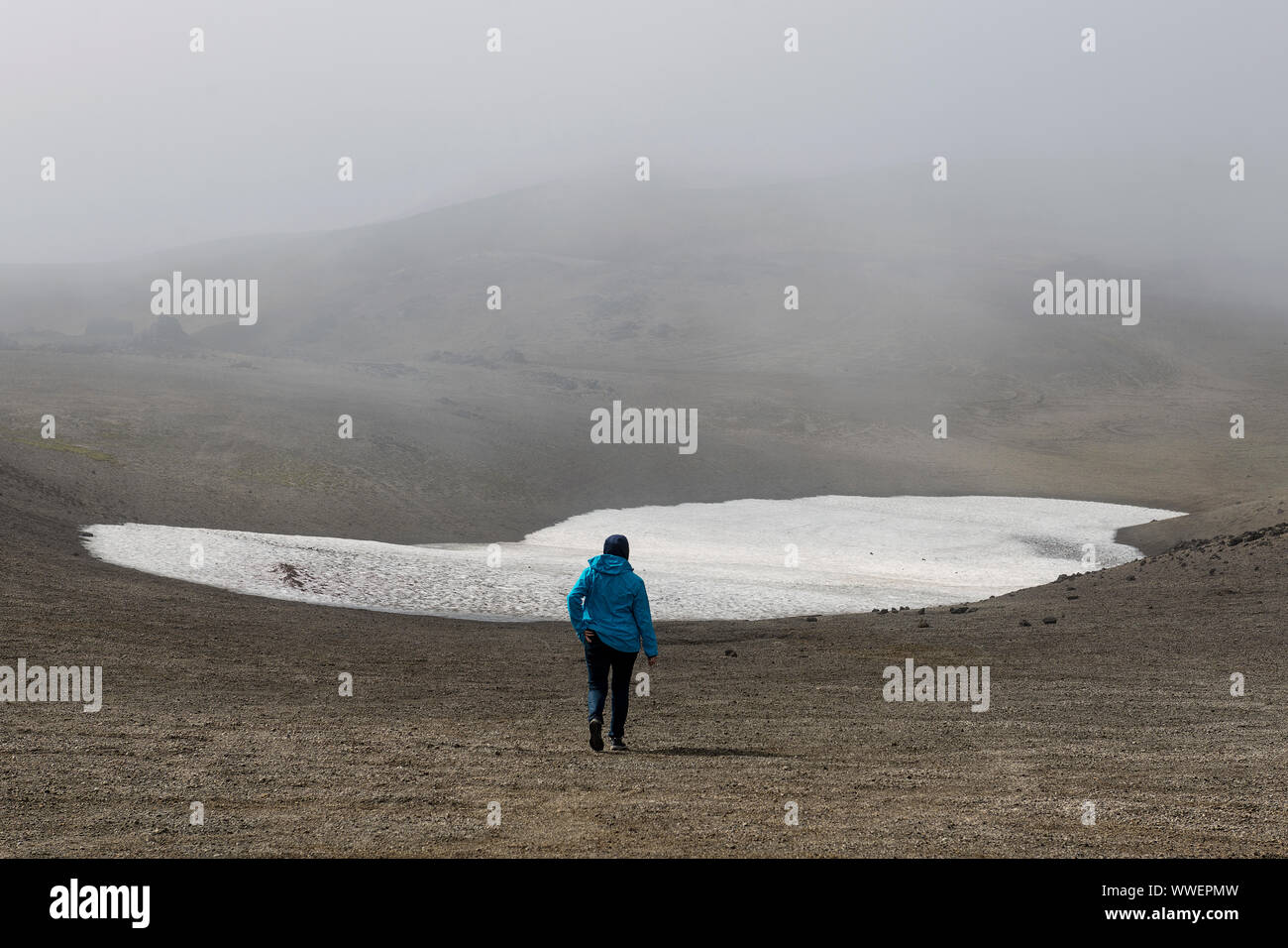 Escursionista singolo che cammina sulla lingua del ghiacciaio Snaefellsjoekull durante l'estate e indossa una giacca blu Foto Stock