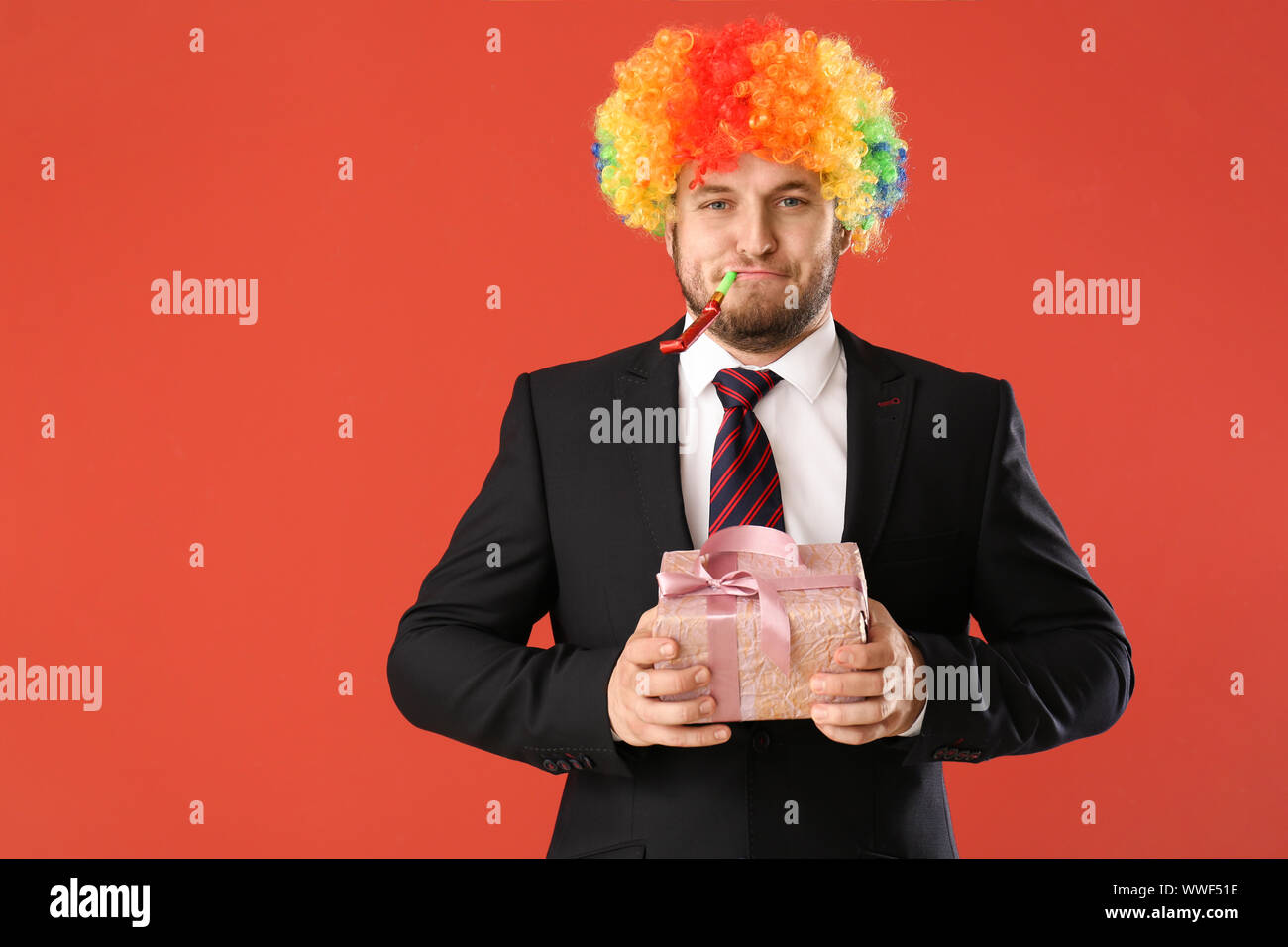 Imprenditore divertenti in arcobaleno parrucca e con il dono sul colore di sfondo Foto Stock