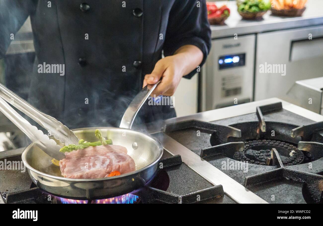 Close-up di un pasto essendo disposti su un settore industriale la stufa del gas da una femmina professionale chef in un ristorante di cucina nelle Filippine. Nessun volto visibile. Foto Stock