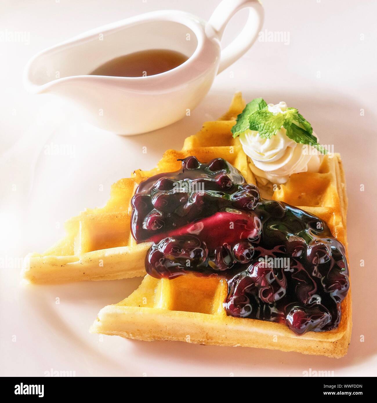 Un bel waffle belgi serviti con mirtillo Frutta sciroppata e panna montata, guarnito con una foglia di menta. Lo sciroppo d'acero sul lato. Foto Stock
