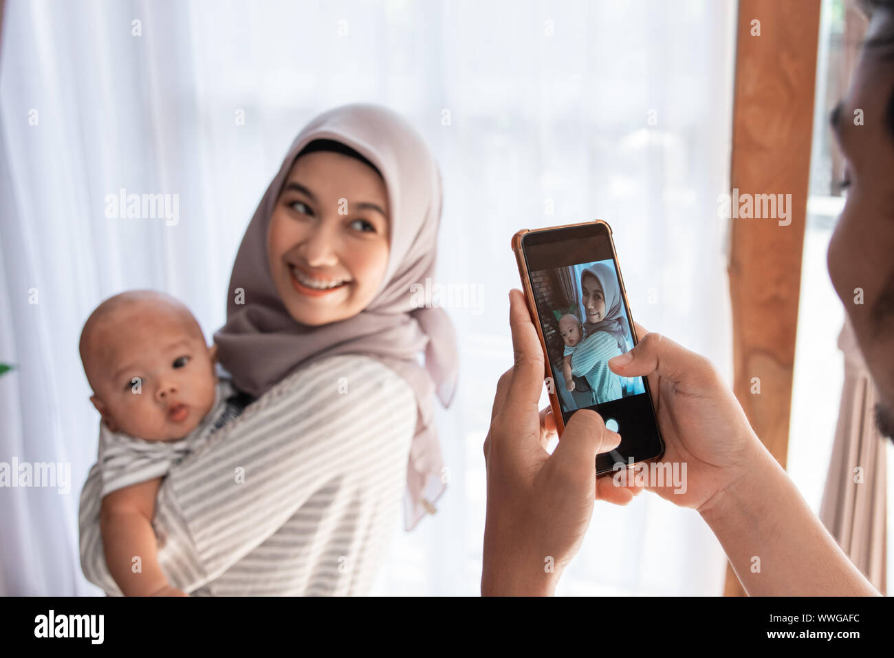 Padre tenendo la foto del suo bambino neonato a casa pur essendo portati dalla madre. parenting musulmano Foto Stock