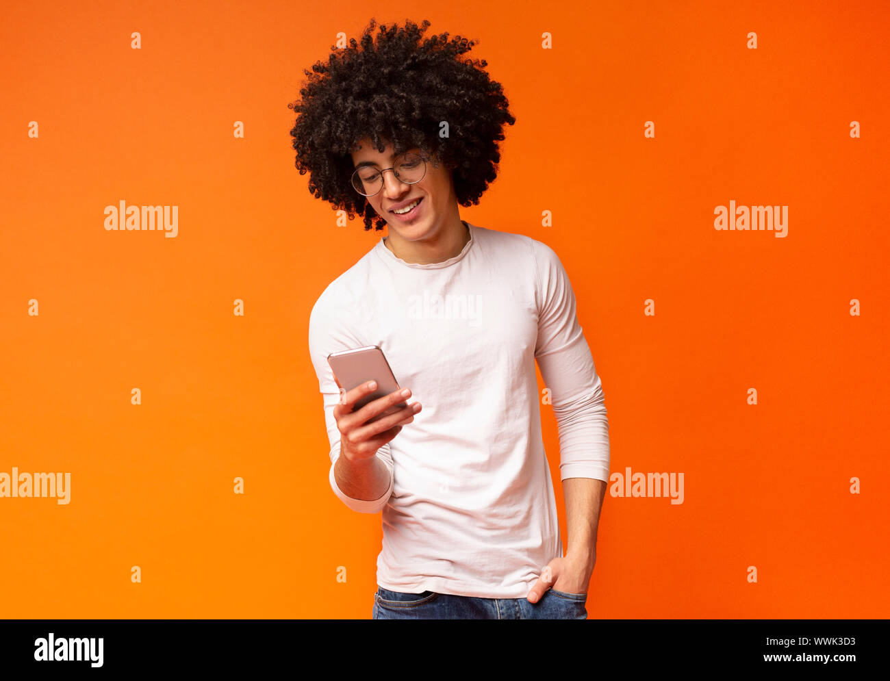 Giovane uomo nero utilizza lo smartphone su arancione di sfondo per studio Foto Stock