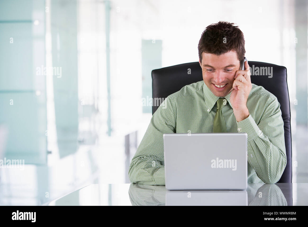 Imprenditore seduto in ufficio utilizzando un telefono cellulare e il computer portatile Foto Stock