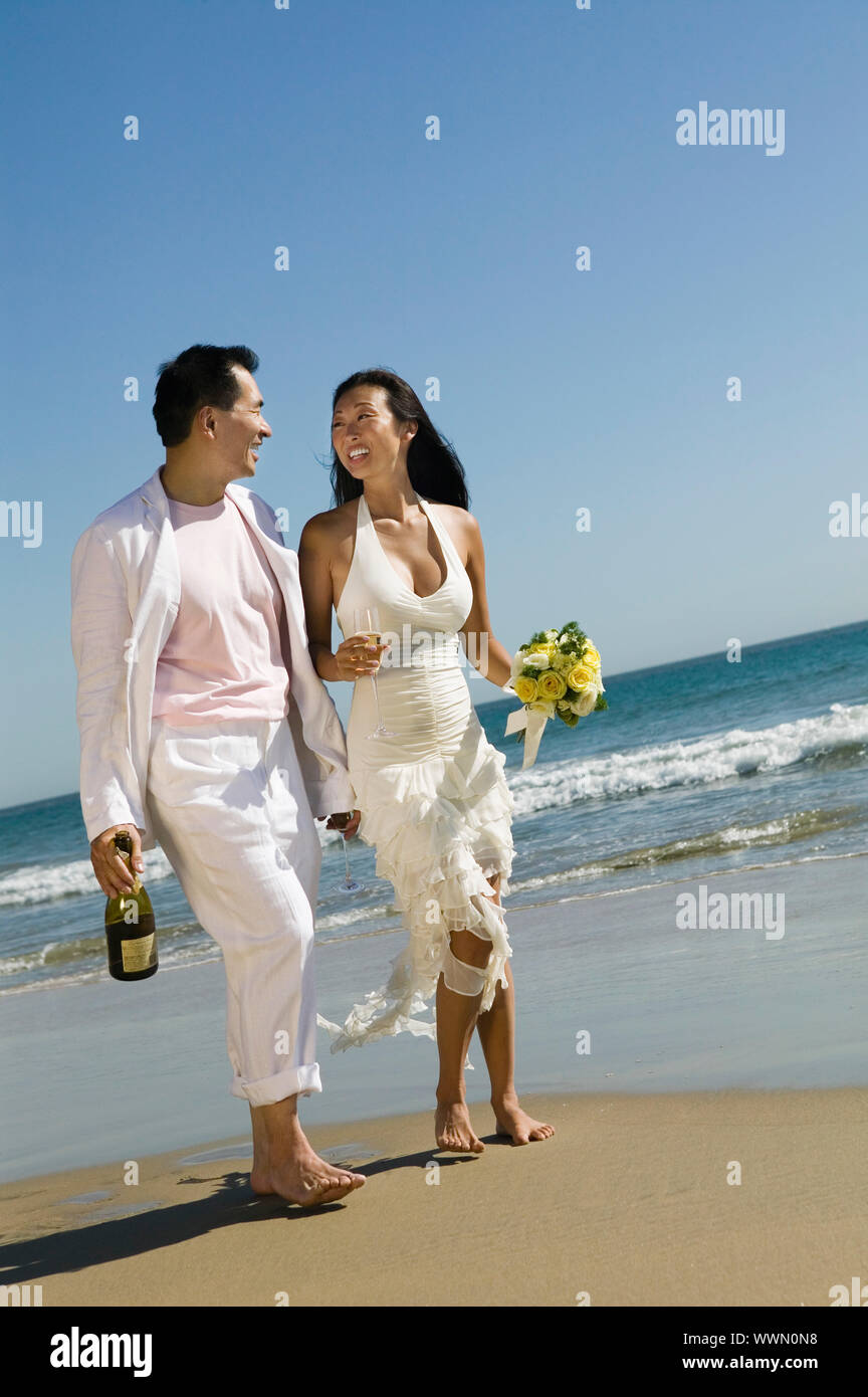 Gli sposi di camminare sulla spiaggia con Champagne Foto Stock