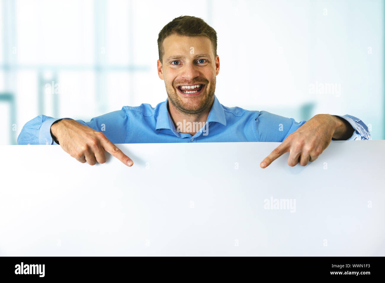 Giovane uomo sorridente puntando su bianco blank board con spazio di copia Foto Stock