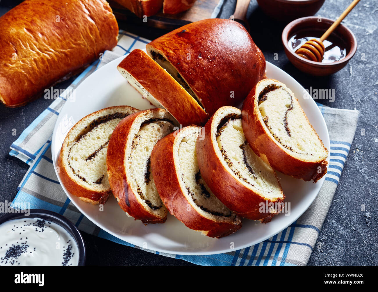 Close-up di una deliziosa torta di papavero, Makovnjaca, dolce pasta lievitata involtino con semi di papavero il riempimento, a fettine su una piastra bianca su una tavola di cemento, Croazia Foto Stock