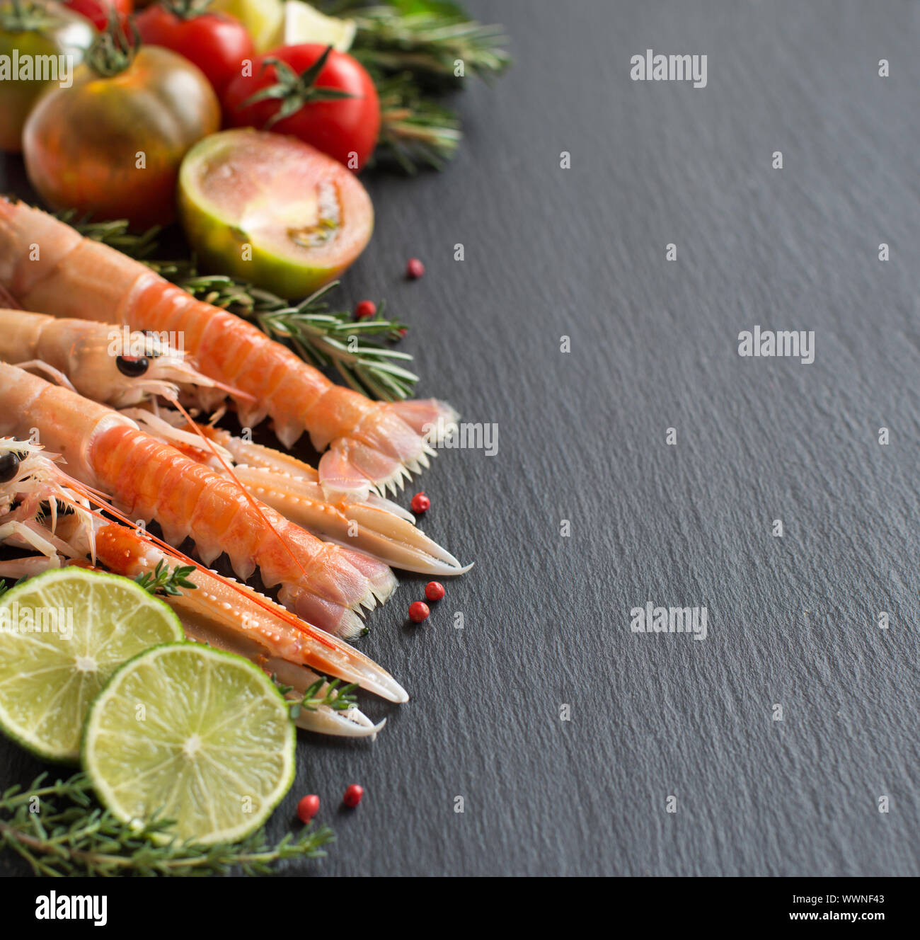 Materie gli scampi con le verdure e le erbe su sfondo scuro Foto Stock