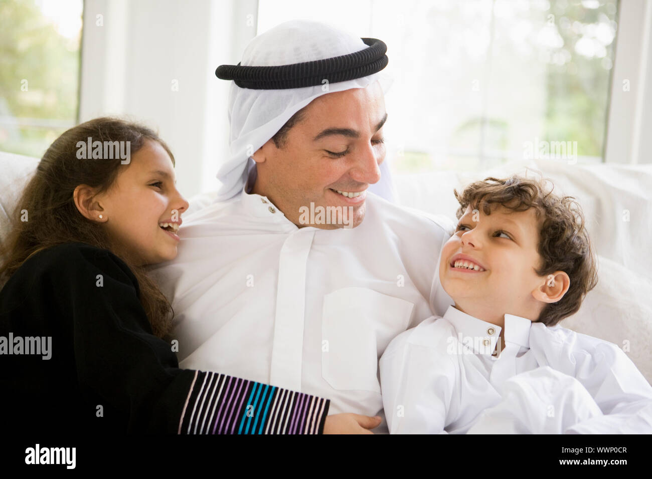 Padre e due giovani bambini seduti in salotto sorridente (alta chiave/messa a fuoco selettiva) Foto Stock