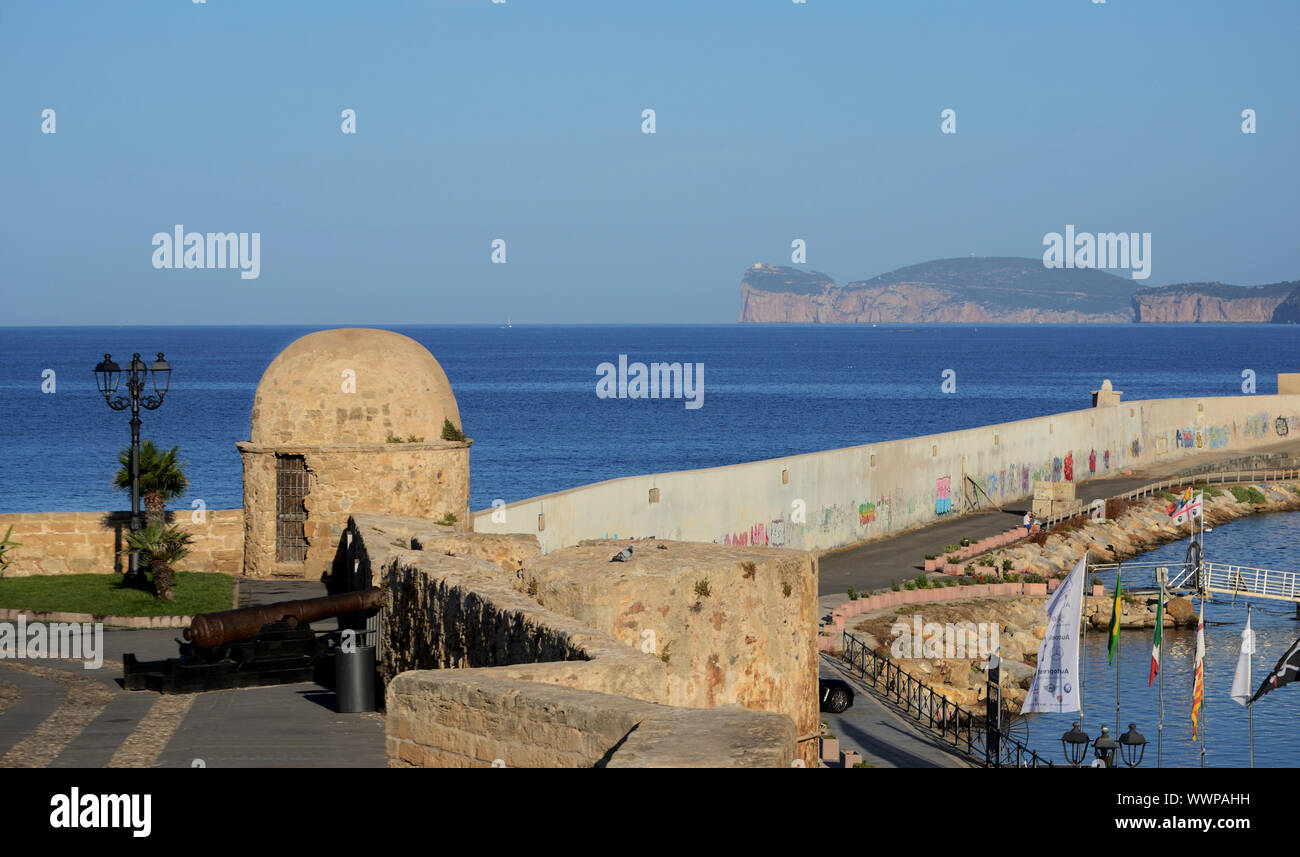 Vista panoramica della città di Alghero, in Sardegna, con le antiche mura in primo piano, il molo del porto e di Capo Caccia cliff sullo sfondo Foto Stock