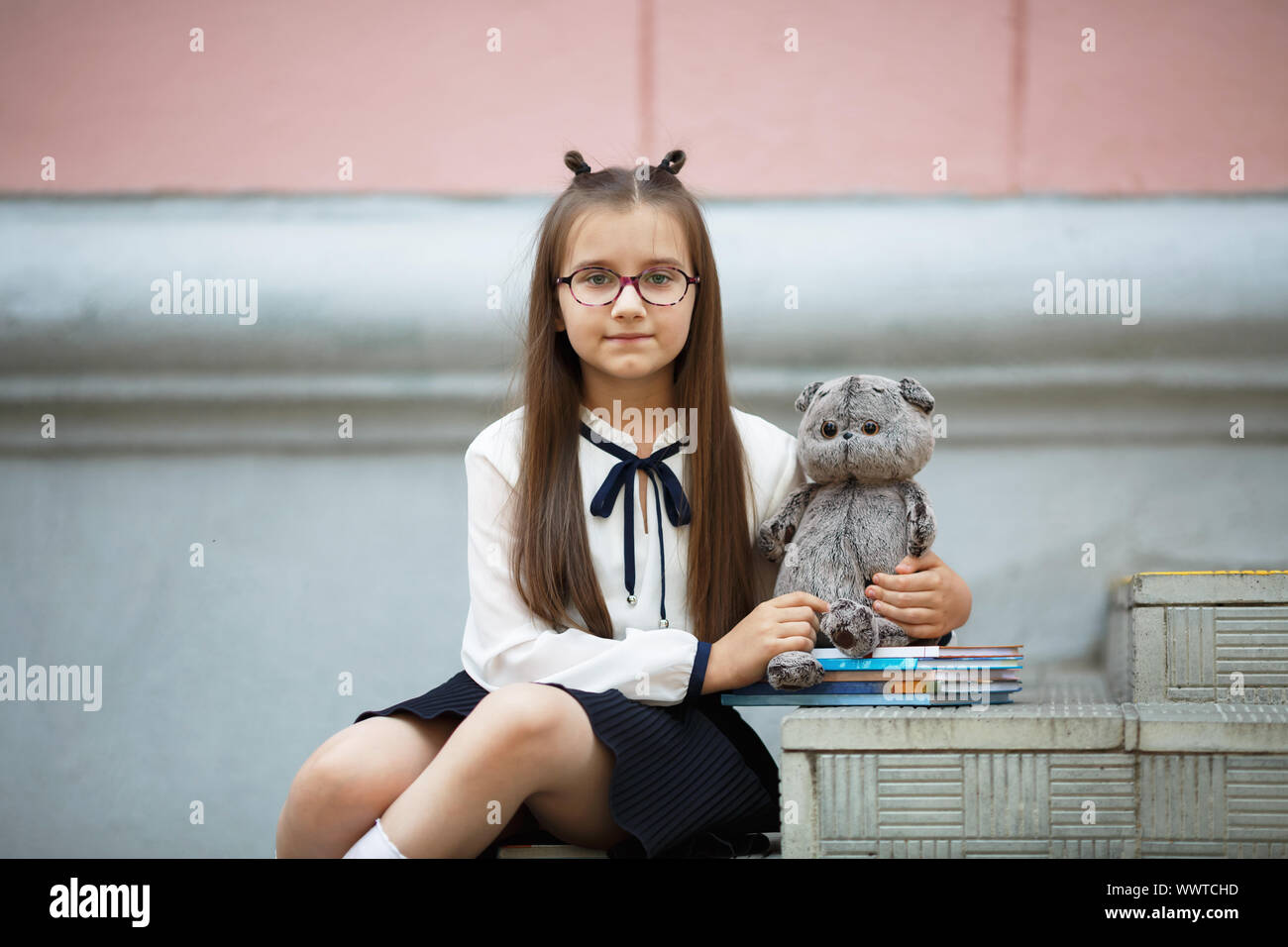 Bambino ragazza con il giocattolo di peluche e libri di testo si siede sui gradini della scuola di scale. Schoolgirl ritratto. Messa a fuoco selettiva. Foto Stock