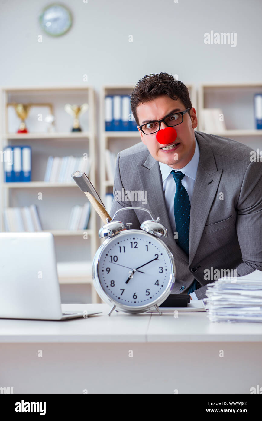 Imprenditore clown in ufficio con un'ascia e sveglia Foto Stock