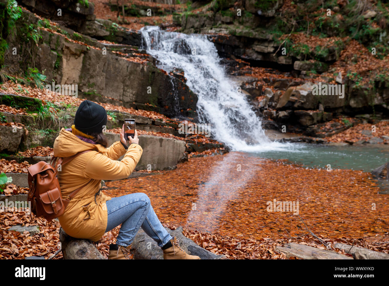 Donna seduta sul log guardando a cascata la stagione autunnale Foto Stock