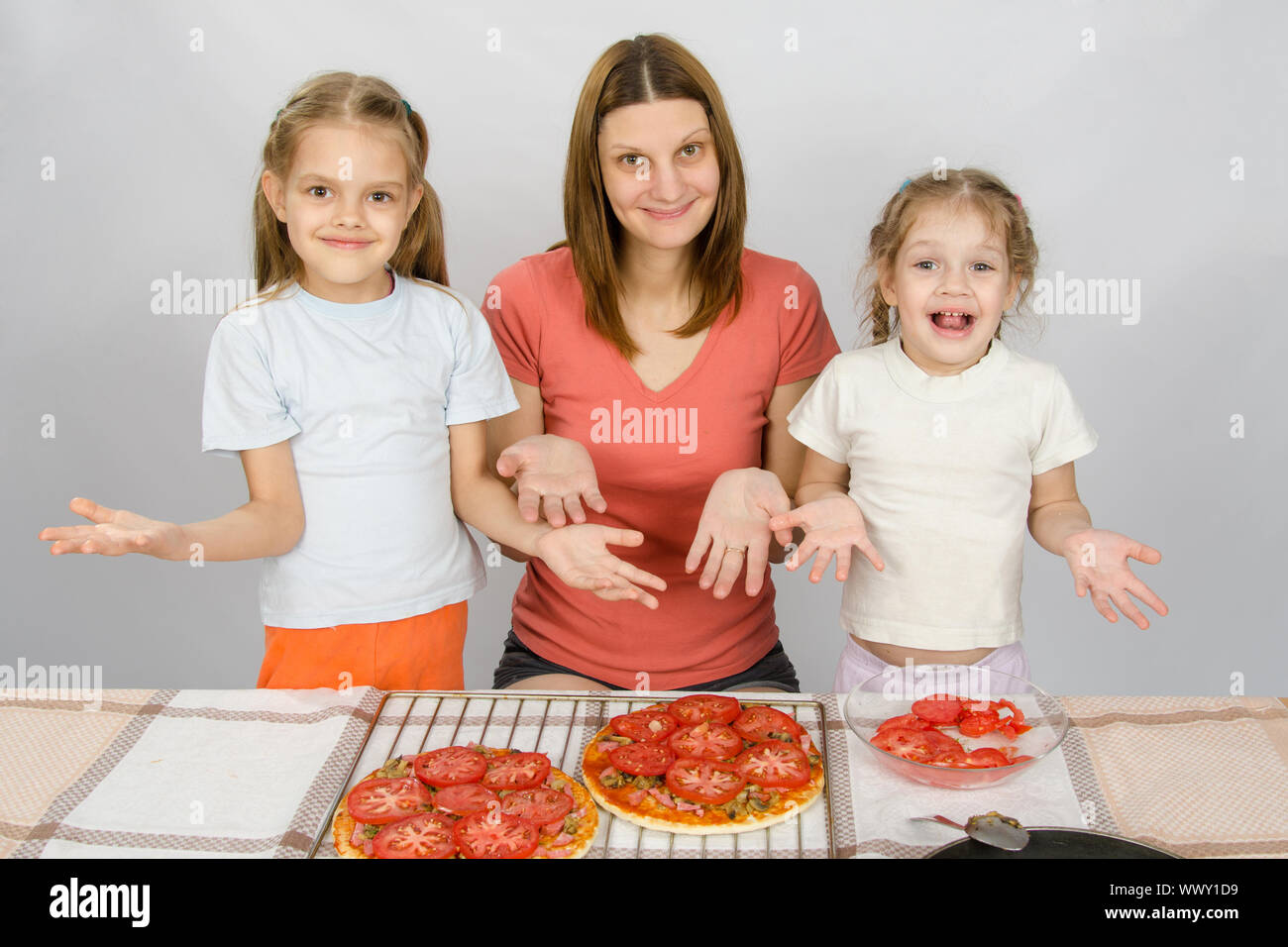 La mamma con le sue due giovani figlie felicemente spettacolo fatto la pizza con pomodori Foto Stock