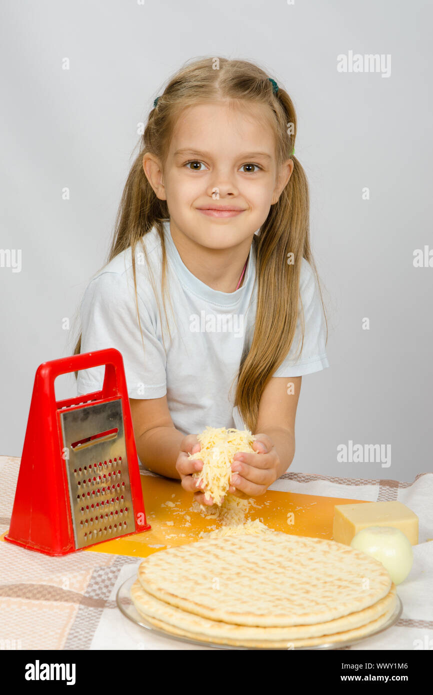 La bambina al tavolo sfregato il formaggio grattugiato per pizza Foto Stock