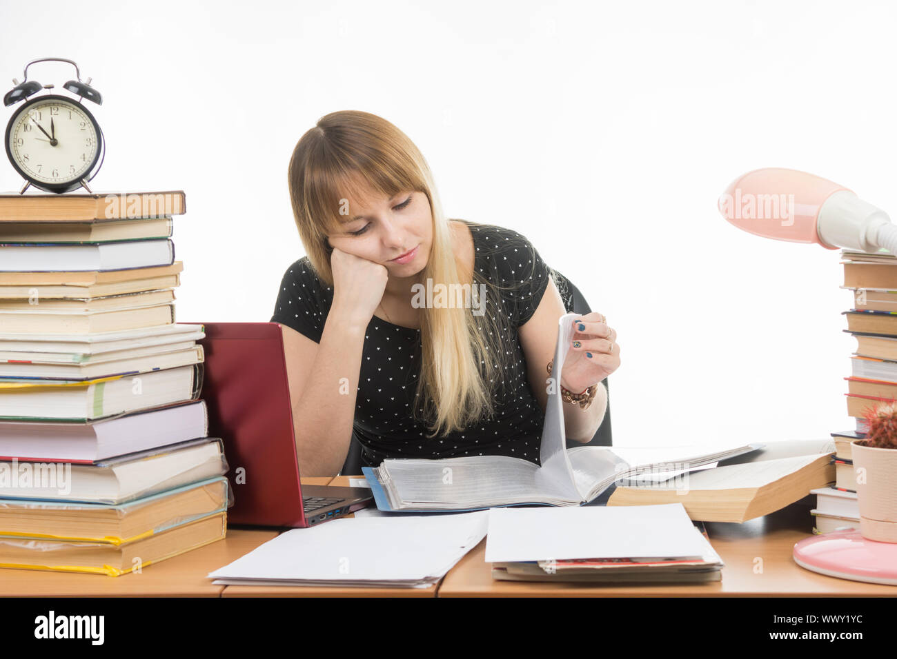 Studente tristemente guardando girando le pagine in una cartella presso il desk tra le pile di libri Foto Stock