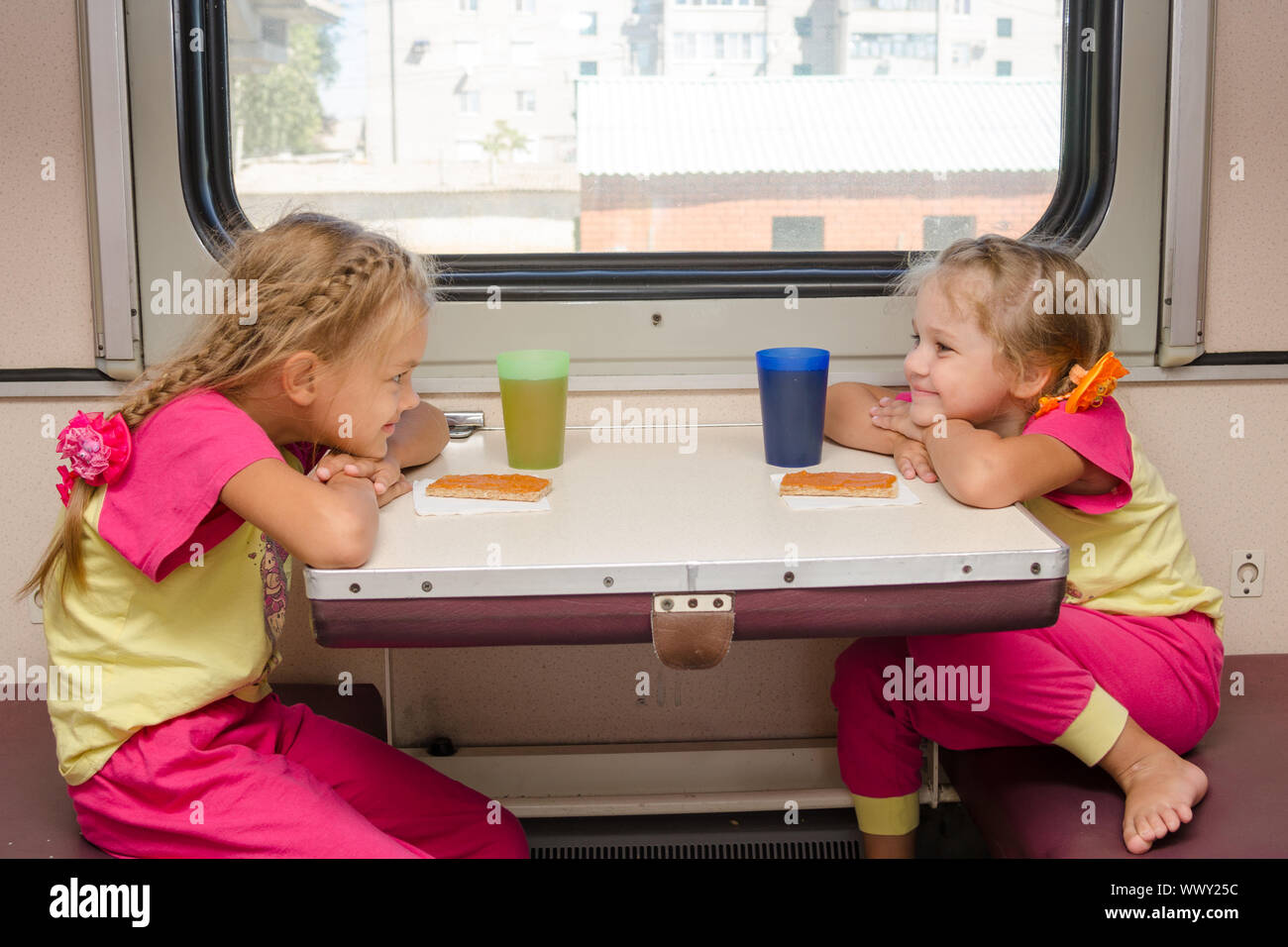 Due bambine con un volto felice guardando ogni altro sul treno seduto al tavolo su esterno della seconda classe di trasporto Foto Stock